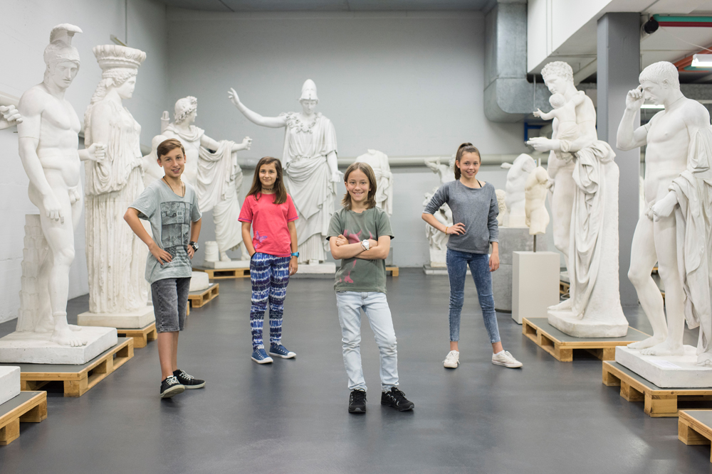 Vier Kinder stehen vor Statuen